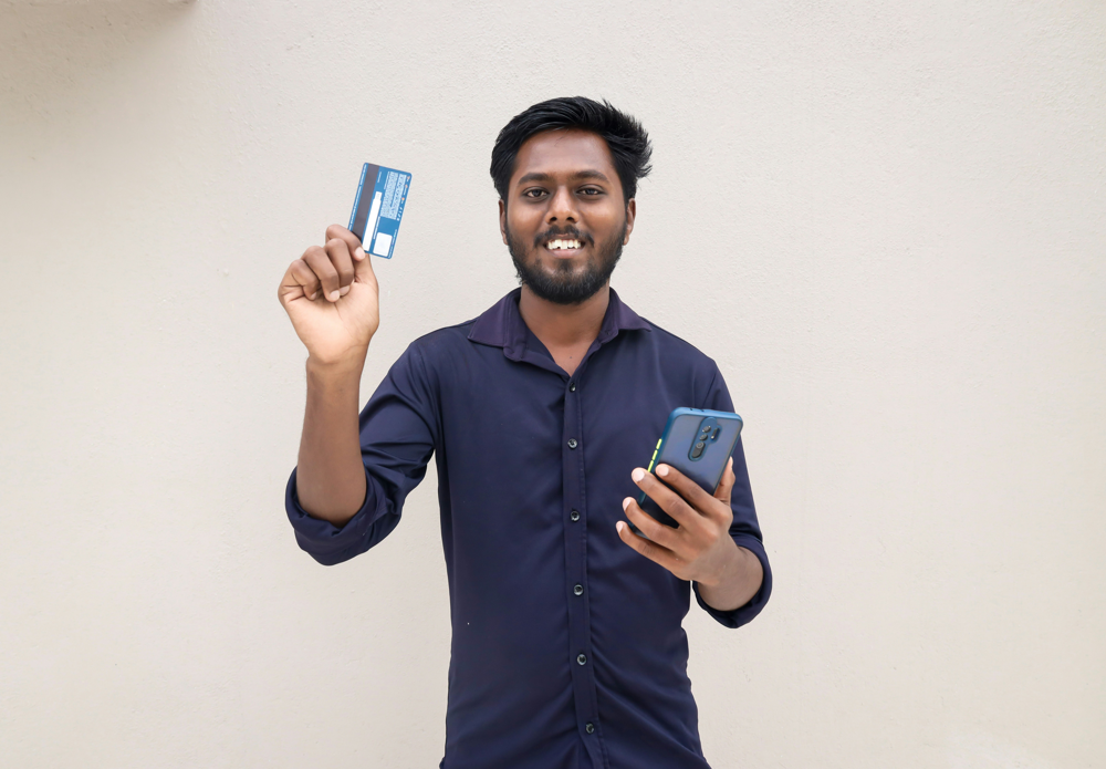 Man holding a debit card and smartphone ready to make a UPI-based payment.