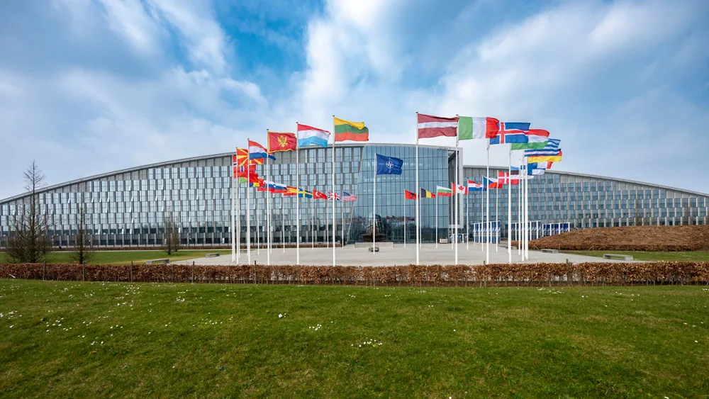 The NATO headquarters building with flags of member countries in front.